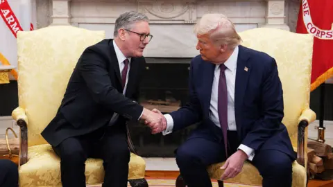Keir Starmer shakes the hand of Donald Trump as they both sit on white chairs wearing suit and tie in the Oval Office at the White House in February