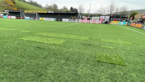 A football pitch with patches where parts have torn or created holes.