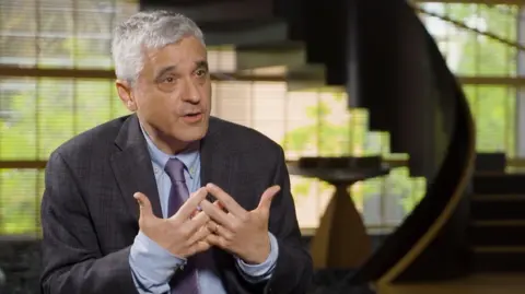 Steven Levitsky wears a grey suit with blue shirt speaking inside a room