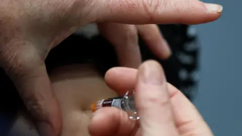 Reuters A pair of hands holding a needle which is going into an arm. 
