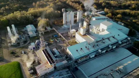 Richard Storey Photography Plumes of steam rise from the cooling towers of a factory complex, seen from above.