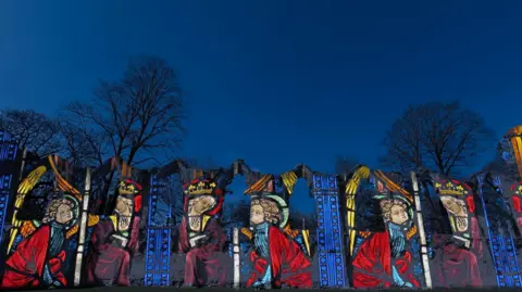 A light show of medieval images in blues and red against the background of medieval abbey ruins