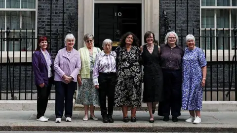 WPA Pool/Getty Images Seven campaigners pose for a photograph after a meeting with British Prime Minister Keir Starmer to discuss historical forced adoption, outside 10 Downing Street on July 02, 2026