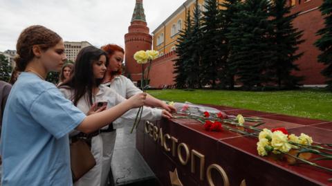 People lay flowers as tribute to the victims of Sunday's attack on a memorial bearing the word Sevastopol in Moscow
