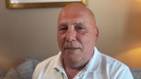 A photograph of Wayne Birkett wearing a white polo shirt