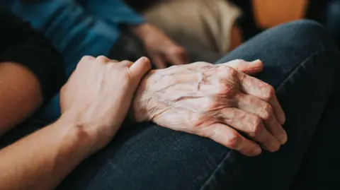Younger person holds an older person's hand.