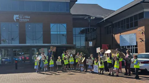 Alec Doyle Pupils and teachers outside the council building wearing yellow hi-vis jackets and holding placards.