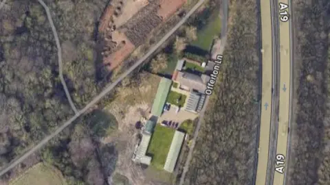 Google A satellite image shows the roofs of several buildings at the kennels' land. It is near Offerton Lane and it is surrounded by trees. The A19 is parallel to the site.