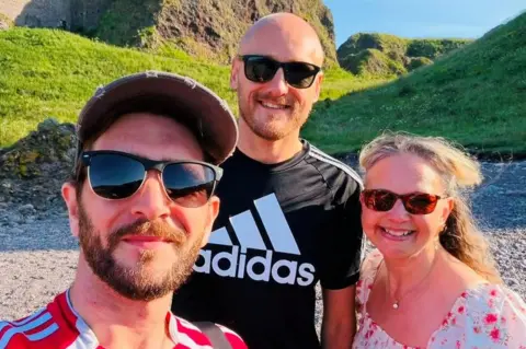 Wish Ambulance Scotland Kieran Hutcheon, Dan Bickmore and Karen Gill, they are smiling at the camera at a beach setting.