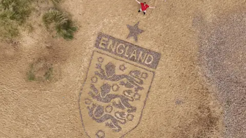 Joe Giddens/PA Wire An aerial image of a large England crest on a beach which has been made using stones and pebbles. 
