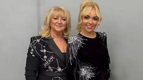 Chantelle Joseph Jane and Chantelle Joseph are standing side by side in front of a grey-painted wall. They are both wearing black dresses with silver embellishments. 
