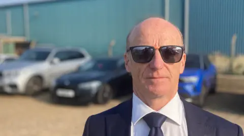 Luke Deal/BBC Kevin Keable of the East of England Energy Group is pictured wearing dark sunglasses while wearing a navy suit, white shirt and navy tie. 