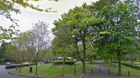 General view of Willenhall Memorial Park. There are several green-leafed trees around grey paths.