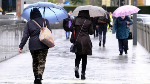 Getty Images Pedestrians walk during a rainfall, holding umbrellas.
