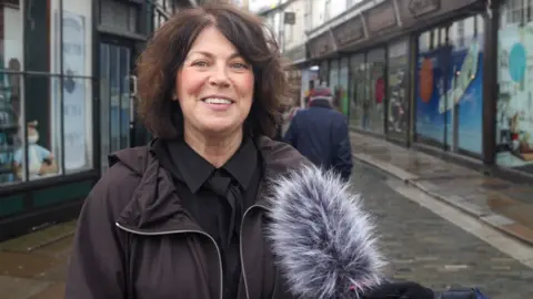 Woman in black shirt and tie and black coat who says she is Sarah Mullally's niece