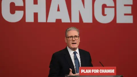 Getty Images Sir Keir Starmer giving a speech on a podium with the words "Plan for Change" on the lectern (red background and white font). The slogan is also the background behind him - only change is visible.