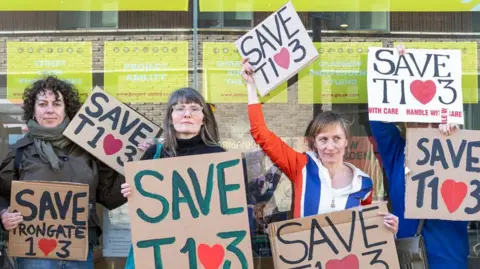 Kirsty Anderson A group of protestors standing outside an art gallery type building. They are all holding signs protesting against possible closure.