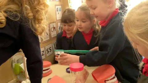 BBC A group of school children around a table playing with a giant toothbrush and big teeth.