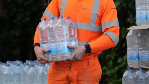A South East Water worker in an orange hi-vi suit hands out bottled water