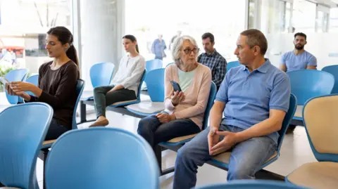 Six people are sat in a GP waiting room