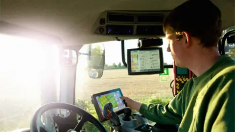 Henry Arden/Getty Man driving tractor with GPS