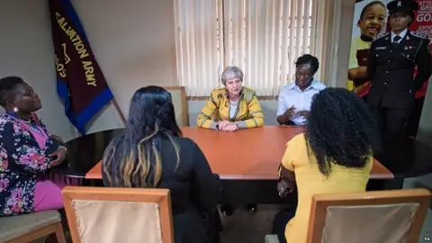PA Theresa May speaks to two women at the Salvation Army headquarters in Lagos