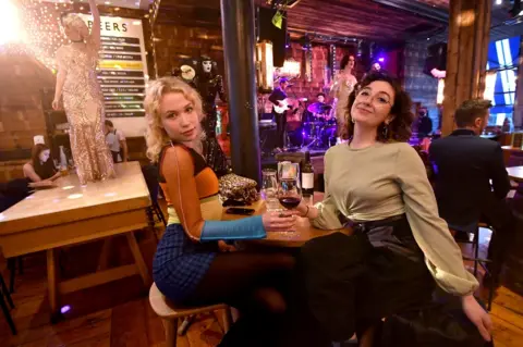 Getty Images Two woman smile at the camera as they enjoy a live show in a bar in Manchester on 17 May, following the easing of lockdown restrictions