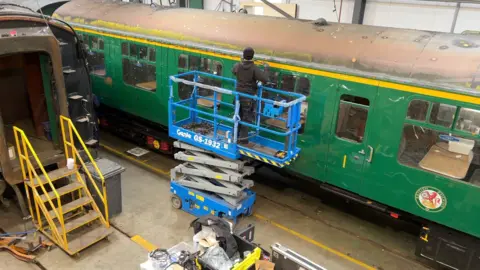 A man is placing LED lights along the side of a train carriage in a workshop.