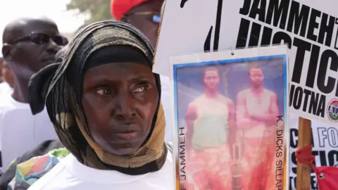 A woman holds up a poster of victims of Yahya Jammeh's regime during a protest in 2020 calling for him to be brought to justice 2020. 