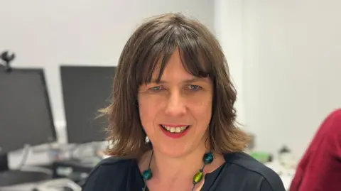 George King/BBC A head shot of Emma Taylor. She has shoulder length brown hair and is looking straight into the camera.