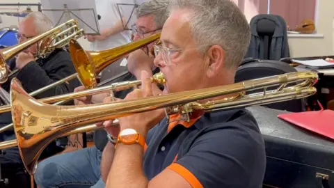 Indian Queens Band A man plays a trombone in a brass band rehearsal room.