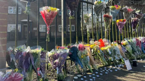 Colourful flowers in a row along some railings and tied to the top of the railings. there are a number of tea lights on the ground. 