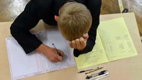 Generic view, looking down at a male student working at a desk, resting his head in his hand