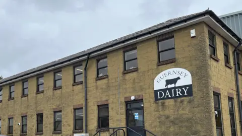 A view of the outside of the dairt. It is a building constructed or light yellow bricks 