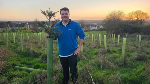 Swindon Borough Council A man in a blue jumper stands next to a sapling