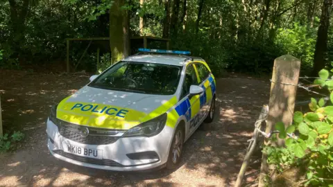 An empty police are parked in woodlands.