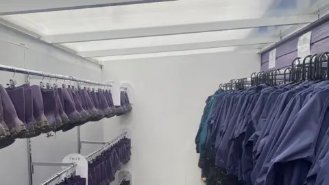 St Augustine's Academy A white room with silver metal rails on both sides. On the left are hooks with loads of pairs of purple wellies, and on the right side are purple raincoats.