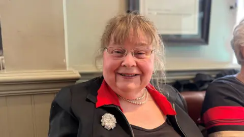 Diana is wearing pearl necklace and a black jacket with red collar