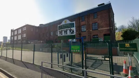 A large three storey red brick school building with a fence in front.