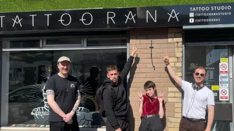 Bianca Oliveira Bianca Oliveira with Michael Socha (both in centre) with two members of crew either side. They all point up to the sign above her tattoo shop reading Tattoorana.
