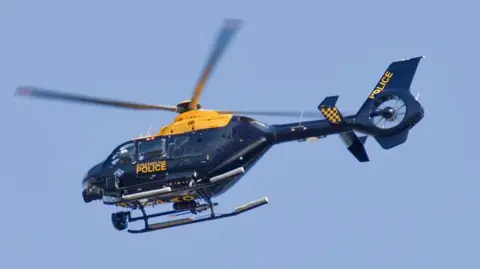 Strathclyde Police helicopter, Eurocopter EC135, rising from the Glasgow Heliport against a clear blue sky. The navy and yellow colours are used by all UK police forces. Personnel can be seen through the windows.