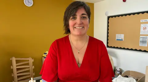 Holly Rattley Woman in red top standing in nursery setting play room 