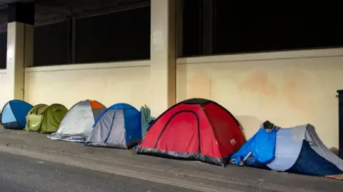 Small, personal-use tents of various colours and sizes set up on a footpath. 