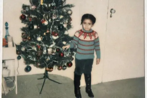 Family handout Five-year-old Andrea is wearing a bright festive jumper and standing next to a Christmas tree in what appears to be a living room. 