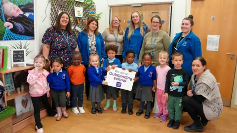 City of Wolverhampton Council Children are celebrating Low Hill Nursery's Outstanding Ofsted judgment. They are pictured with, left to right, Natalie Showell, Headteacher, Runak Hamad, UQT, Emma Harris, SENCO, Hayley Tipple, Early Years Practitioner, Tara Smith, Pastoral Support, Toni Jones, Early Years Practitioner, and Samantha Phillips, Pastoral Support.