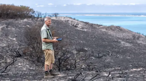 A man standing in a scorched heathland after a wild fire