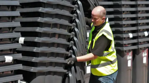 Wokingham Borough Council Man in hi vis jacket pushing a stack of black wheelie bins
