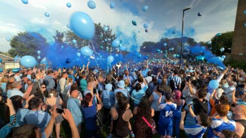 Blue balloons and smoke canisters being released into the sky 