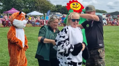 CLAIRE WHITEWAY Claire, smiling, while being fastened into a black-and-white cow costume. 