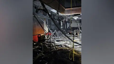 Stockton Borough Council A room with blackened panel walls, metal piping hanging from the ceiling, and furniture strewn across the floor. 